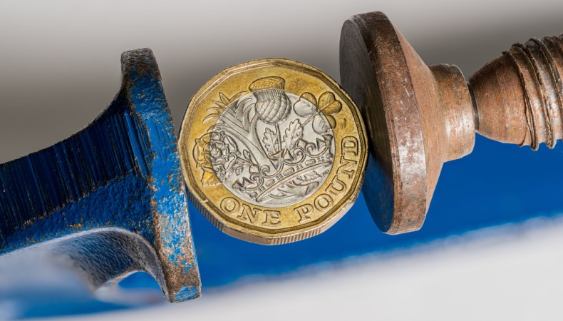 A pound coin being squeezed between two bars